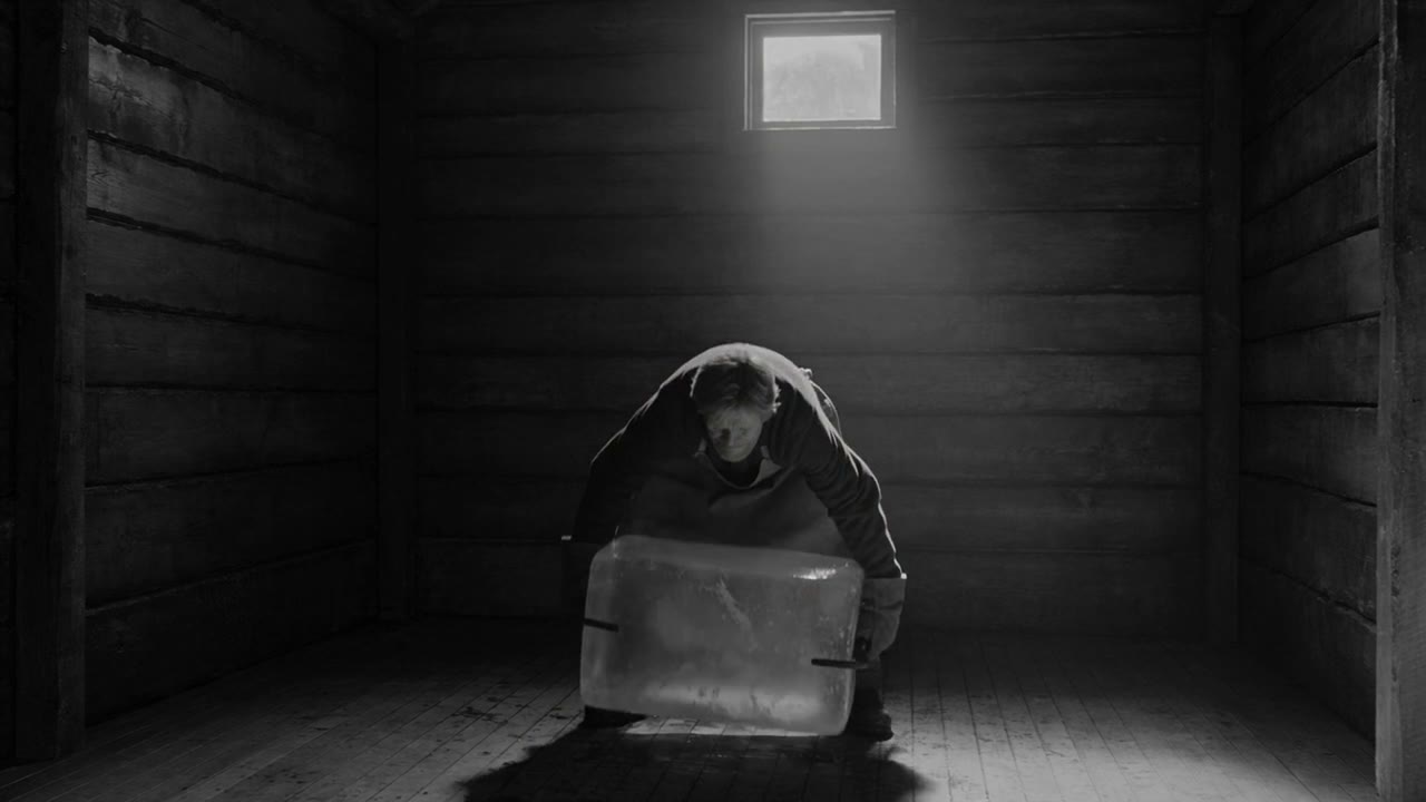 An ice man lifting a block of ice in a dark ice house